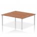 This photograph features a sleek and modern office bench desk with a silver frame and walnut top. It is designed for two people and offers a dynamic and efficient working space. The clean lines and simple design make it a stylish addition to any office.