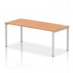 The picture shows a modern office space with a sleek silver-framed bench desk in the foreground. The desk has a glossy oak top and is part of a single row of dynamic bench desking. The overall look is clean, efficient, and professional.