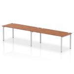 The photograph shows a dynamic bench desking system with an Impulse Bench Single Row that can accommodate 2 people. The frame is silver in color and the desk is made of walnut wood. Perfect for a modern and collaborative office setting.