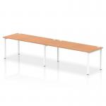 The photograph depicts a sleek and modern office bench desk, with two people seated at the Dynamic Bench Desking Impulse Bench. The desk features a 1800 white frame and is topped with an oak wood surface. The single row design creates a dynamic workspace for collaborative productivity.