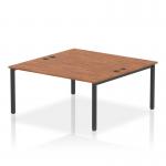 This photograph captures a sleek and modern office space with two B2B dynamic bench desks in black and walnut. The desks are connected by a shared black frame, providing ample workspace for two people. The smooth lines and contemporary design make this an ideal setup for any fast-paced and collaborative office environment.