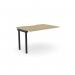 The photograph shows an urban oak bench desk with add-on units, scallop top, and black accents. It comfortably accommodates one person and measures 1200 x 800. The C-sense 1 person add-on unit seamlessly blends with the desk, creating a sleek and functional workspace.