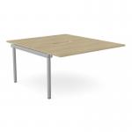 The photograph shows a sleek and modern office bench desk with add-on units. The desk features a scallop top and is 1400 x 800 in size, made with a stylish urban oak finish. It is designed for 2 people and includes a silver SLV panel for added functionality.