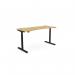 The photo shows a rounde height-adjustable desk with a rectangular bamboo top and black frame. The desk is 1600x700mm in size and can be used for sitting or standing while working. The design is simple and modern, making it a great addition to any office space. The bamboo top adds a touch of warmth and sustainability to the overall look.