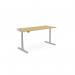 The picture shows a stylish and functional office setup, featuring a round, height-adjustable desk with a 1600 x 700mm rectangular bamboo top and a silver frame. The desk allows for both sitting and standing positions, providing ergonomic support and versatility.