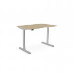 In this picture, there is an Edit Office Sit Stand and Height Adjustable Desk. It features a double purpose scallop design and measures 1200 x 800mm. The frame is silver and the desk has an urban oak finish. The desk is in a raised position and has a round shape.