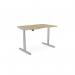 In this picture, there is an Edit Office Sit Stand and Height Adjustable Desk. It features a double purpose scallop design and measures 1200 x 800mm. The frame is silver and the desk has an urban oak finish. The desk is in a raised position and has a round shape.
