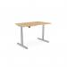 The photo shows a versatile office desk with a round shape and a double purpose scallop. It is height adjustable and can be used while sitting or standing. The desk has a beech top and a silver frame, measuring 1400 x 800mm.