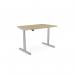 The picture shows a modern and functional office setup with Edit Offices Sit Stand and Height Adjustable Desks. The round-shaped desk features an Urban Oak tabletop and a sleek Silver frame, with built-in Alu Portals for convenient cable management. The desk measures 1200 x 800mm and is ideal for any contemporary workspace.