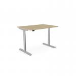 The picture shows an office workspace with a round height adjustable desk, featuring an urban oak top and a silver frame. The desk also includes aluminum portals and measures 1400 x 800mm. The modern design provides a versatile and ergonomic workspace for any office setting.