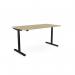 The photo shows an office space with a round height-adjustable desk, featuring an urban oak top and black frame. The desk has an aluminum portal for cables and measures 1800 x 800mm. It offers both sitting and standing options for customizable comfort.