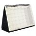 The photo features a sleek, black Sigel Conceptum Desktop Planner for the year 2026. The cover is embossed with subtle patterns and the planner opens to a month-to-view layout. Its compact size of 300x143x18mm makes it perfect for any desk or workspace.