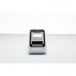 This image features the Brother QL-820NWBC Desktop Label Printer 33300J from Brother Label Makers. The printer is white with a sleek, modern design. It has a compact size and a large, easy-to-read screen. The label maker is shown with a roll of labels inserted and a user pressing buttons on the screen.