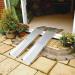 In the photograph, two slender, silver metal ramps extend outward from each other, creating a sturdy and accessible pathway for vehicles. The ramps are made from durable aluminium and feature telescopic folding channels.
