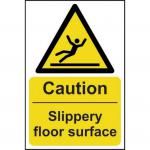The photo shows a bright yellow Spectrum Industrial Caution Slippery Floor Surface Sign with black text in 200mm x 300mm size. The self-adhesive vinyl material makes it easy to stick onto any surface for clear warning.