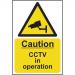 A yellow rectangular sign with bold black text reading Caution CCTV In Operation on the top, and Spectrum Industrial on the bottom. In the center, a large image of a CCTV camera with a red circle and line crossing it out. The sign measures 200mm x 300mm and is made of self-adhesive vinyl material.