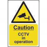 The photograph depicts a Spectrum Industrial CCTV sign, with bold text reading Caution CCTV In Operation on a self-adhesive vinyl material. Measuring 400mm x 600mm, the sign is suitable for use in industrial settings. The design features simple graphics and a clean, professional layout.