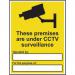 The photo shows a Spectrum Industrial CCTV sign, made of self-adhesive vinyl and measuring 300mm x 400mm. The sign reads These Premises Are Under CCTV Surveillance and features a camera symbol. The black and white design is clear and easy to read.