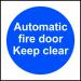 This photograph features a brightly colored industrial fire safety sign with the words Automatic Fire Door Keep Clear in bold letters. The sign is made of self-adhesive vinyl and measures 100mm x 100mm. It is designed to alert individuals to keep the area near the fire door clear at all times.