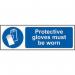 This photo shows a bright yellow sign with bold black letters reading Protective Gloves Must Be Worn on a white background. The sign is made of self-adhesive vinyl and measures 300mm x 100mm. In the center of the sign is a symbol of a pair of protective gloves, emphasizing the message. The sign is from Spectrum Industrials PPE collection and is designed to stand out and be easily noticed.