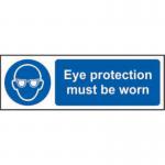 The photo captures a bright yellow industrial PPE sign from Spectrum, featuring bold black lettering that reads Eye Protection Must Be Worn. The self-adhesive vinyl material makes it easy to place on any surface, and the compact size of 300mm x 100mm ensures visibility in any workspace.