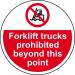 The photograph shows a large, circular floor graphic with the words Forklift Trucks Prohibited Beyond This Point in bold letters. The graphic is anti-slip and laminated for durability. In the background, multiple forklift trucks can be seen. The bright colors and clear font make the message easily visible and attention-grabbing.