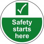 The picture depicts a large, circular floor graphic featuring the words Site Safety Starts Here in bold lettering. The graphic is laminated to prevent slipping and is designed for industrial environments. It also includes a vibrant spectrum of colors to draw attention and enhance safety.