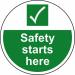 The picture depicts a large, circular floor graphic featuring the words Site Safety Starts Here in bold lettering. The graphic is laminated to prevent slipping and is designed for industrial environments. It also includes a vibrant spectrum of colors to draw attention and enhance safety.