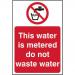 This photograph captures a Spectrum Industrial Prohibited Sign for metered water. The self-adhesive vinyl sign is 200mm by 300mm in size and features the bold message, This Water Is Metered Do Not Sign. The white text stands out against a red circle background, making it easily noticeable and effective in conveying the message.