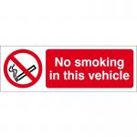 The picture shows a small rectangular sign with bold white lettering on a black background. The words No Smoking In This Vehicle are prominently displayed in the center. The sign is made of self-adhesive vinyl and measures 150mm x 50mm. It is designed to be used in industrial settings to indicate a non-smoking area.