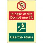The photo shows a Spectrum Industrial Fire Safety Sign with bold red text stating In Case Of Fire Do Not Use Lift Use The Stairs. The sign is made of 1.3mm rigid material and has a self adhesive backing. It also features photoluminescent properties, making it visible in low light conditions. The sign measures 200mm x 300mm and is suitable for industrial settings.