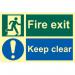 This image shows a Spectrum Industrial Fire Safety Signs Fire Exit Keep Clear Sign. The sign is made of flexible photoluminescent vinyl and measures 300mm x 200mm. It features a bold, red and white design with clear text and symbols, making it easily visible and legible in an emergency situation. The photoluminescent material means that the sign will remain visible even in low light conditions.