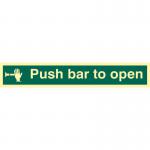 The photograph captures a Spectrum Industrial Fire Safety Signs Push Bar To Open Sign, made of Flexible Photoluminescent Vinyl measuring 300mm x 100mm. The sign is prominently displayed against a white background, with the words Push Bar To Open clearly visible in bold, black font. The vinyl material gives off a faint glowing effect, making it easily visible in low light conditions.