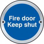 A shiny, circular, metal sign with bold white letters reading Fire Door Keep Shut against a spectrum of colorful stripes. Perfect for industrial settings and fire safety regulations.
