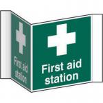The photograph shows a vibrant Spectrum Industrial First Aid Signs sign, specifically a projection sign for a first aid station. It is made of 1.2mm recyclable PP and has a 200mm face. The bright and bold sign is designed to catch attention and clearly indicate the location of a first aid station.