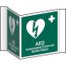 This photo features a bright yellow Spectrum Industrial First Aid sign, with the words AED and First Aid in bold black letters. The sign is made of 1.2mm recyclable PP and has a 200mm face, making it easily visible. The image also shows that the sign is projected outward, making it easy to see from a distance.