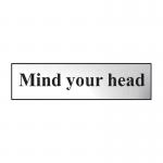 This photograph features a chrome effect Spectrum Industrial Room Sign that reads Mind Your Head in bold font. The sign is made of self-adhesive PVC material and measures 200mm x 50mm. The sleek and modern design is suitable for any industrial setting.