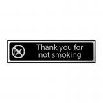 This photograph captures a sleek and modern Spectrum Industrial No Smoking Sign in black and polished chrome effect. The sign features the words Thank You For Not Smoking in bold white font against a black background. Measuring 200mm by 50mm, it is made of self-adhesive PVC for easy installation.