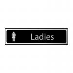 The photograph shows a sleek and modern Spectrum Industrial Washroom Sign for ladies. The sign features a black and polished chrome effect, giving it a stylish and professional look. Made from self-adhesive PVC, the sign measures 200mm x 50mm.
