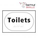 The photograph shows a Spectrum Industrial washroom sign for toilets, with a self-adhesive taktyle design in white. The sign measures 225mm by 150mm and is labeled TK2030BKWH.